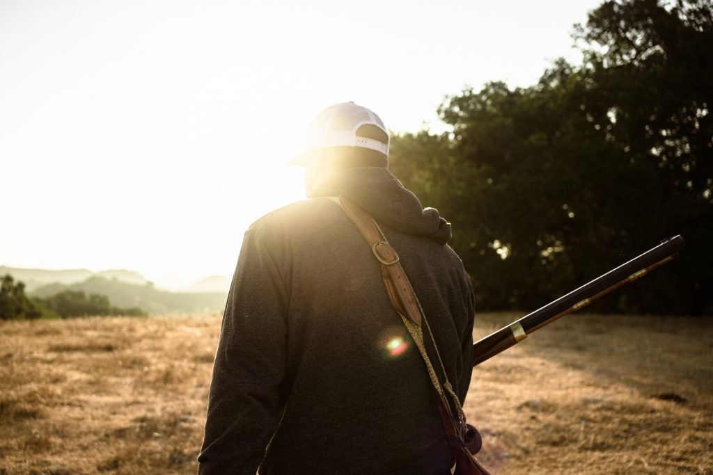 Man with a musket walking towards the mountains in the early morning.